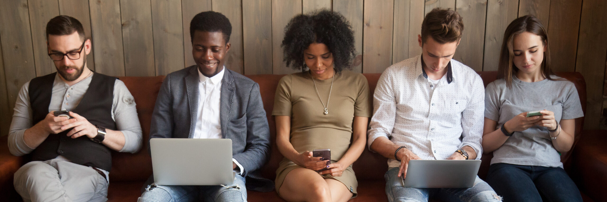 Five diverse people girls guys sitting on couch using mobile phones and laptop to purchase items