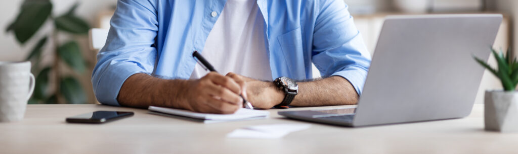 Happy Guy Wearing Headphones Studying Online With Laptop At Home, Smiling Millennial Guy Watching Webinar And Taking Notes To Notepad, Enjoying Distance Learning, Free Space